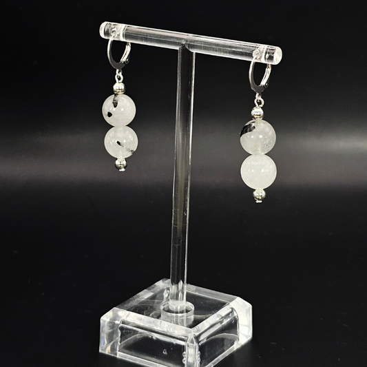 Pair of earrings on a clear stand against a black background