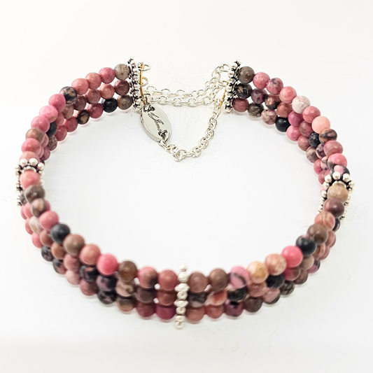 Close-up of a Rhodonite 4 mm triple-strand bracelet featuring three rows of soft pink polished gemstone beads, accented with small silvery spacer rings and a silver-tone adjustable chain clasp, displayed against a clean white background.