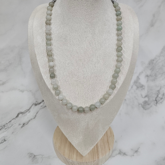 Necklace with green beads on a white stand against a marble background