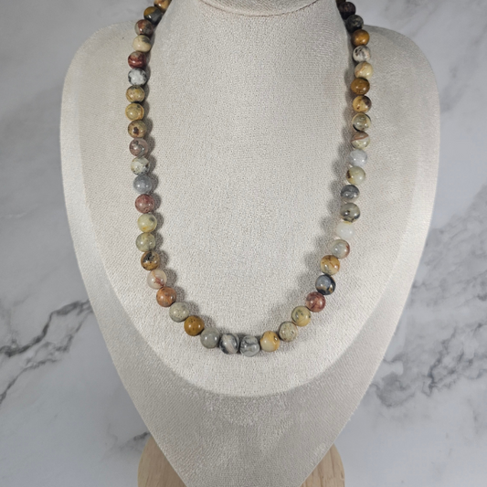 Necklace with multicolored beads on a mannequin bust against a marble background