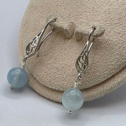 Silver earrings with light blue beads on a textured beige surface