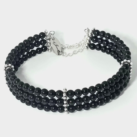 Black Onyx 4mm Triple Strand Bracelet featuring smooth black beads on silver-plated memory wire with a fixed safety chain.