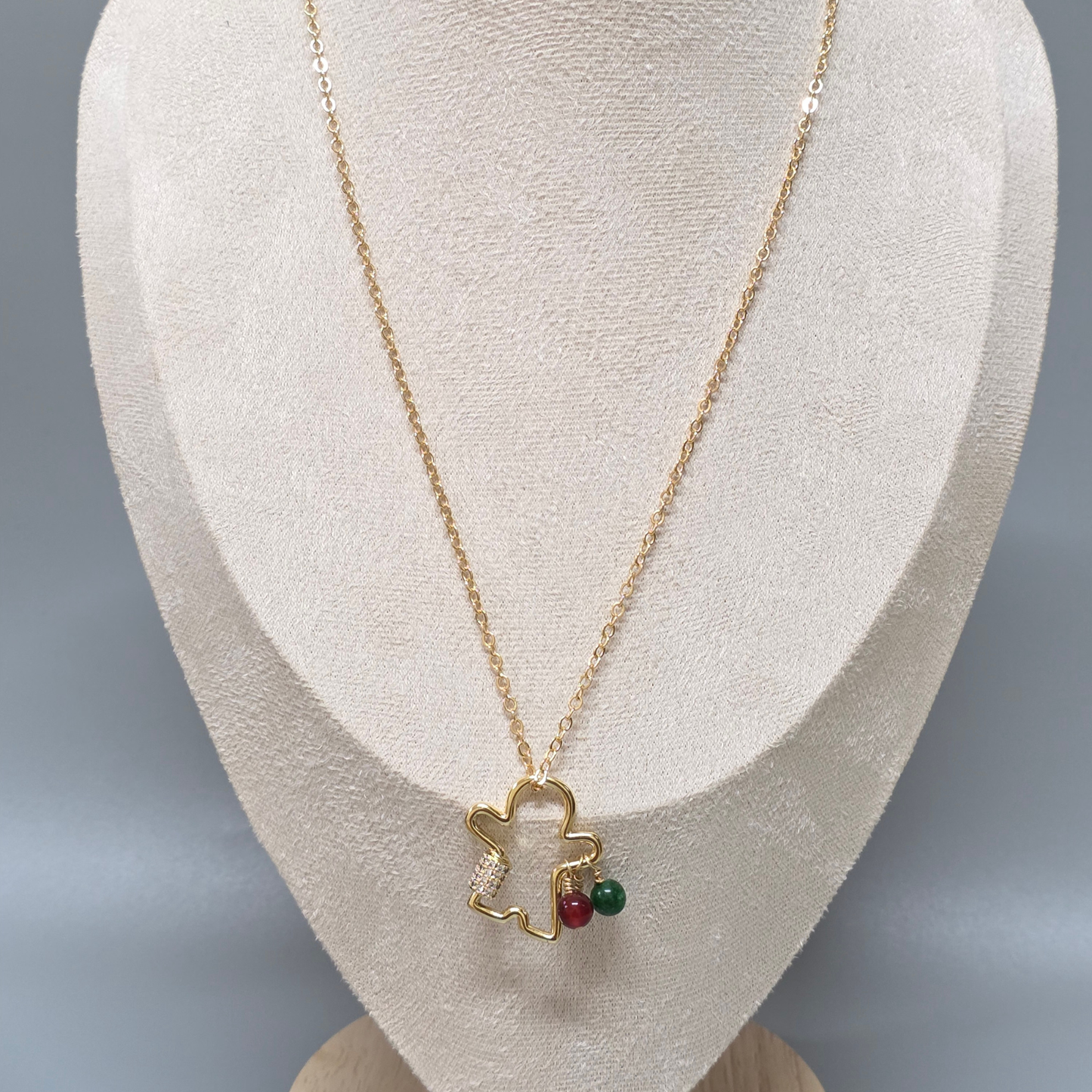 Handcrafted gold gingerbread man necklace with a heart-shaped pendant and red and green beads on a mannequin bust.