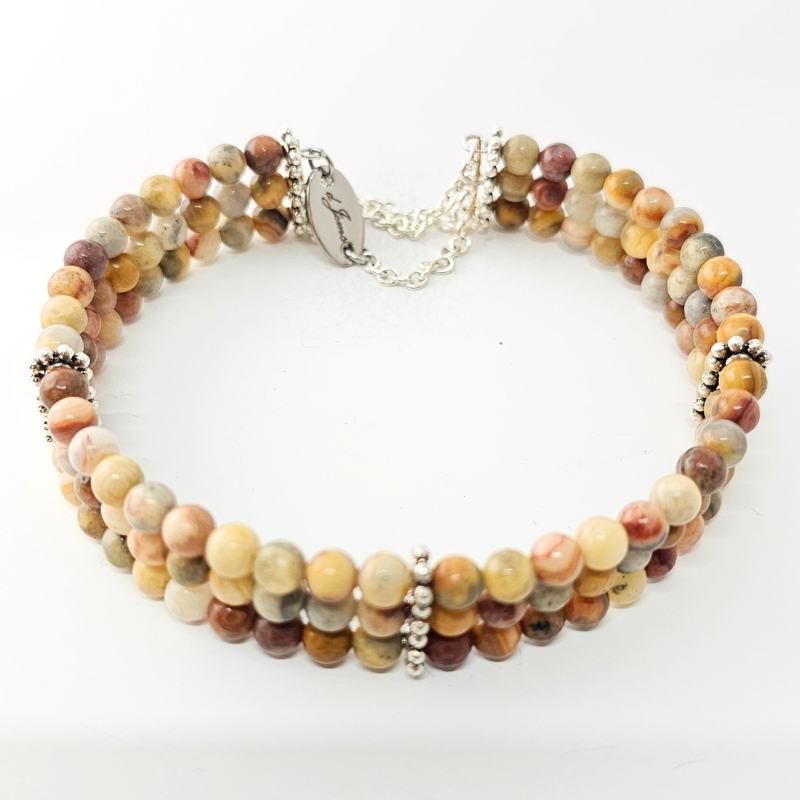 Close-up image of the Crazy Lace Agate 4mm Triple Strand Bracelet showcasing multicolored swirling beads in a triple-strand arrangement.
