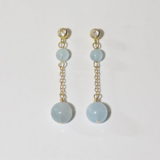 Pair of earrings with light blue gemstones and gold chains on a white background