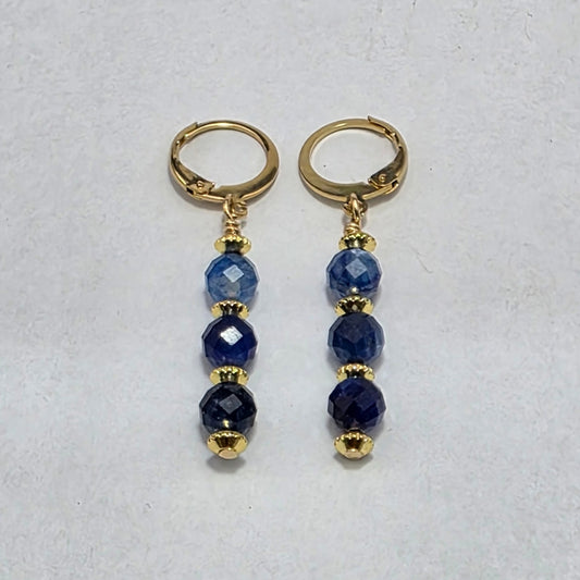 Pair of gold hoop earrings with blue beads on a light gray background