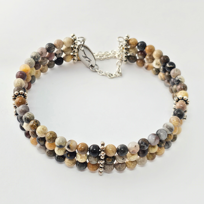 Triple strand bracelet made of 6mm polished multi-colored picture jasper beads, accented with silver-toned decorative spacers and a chain clasp engraved with “Je’Luna.”