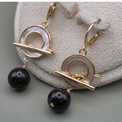 Garnet gold earrings with black beads on a textured surface