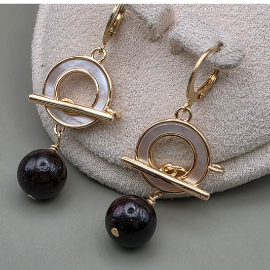 Garnet gold earrings with black beads on a textured surface