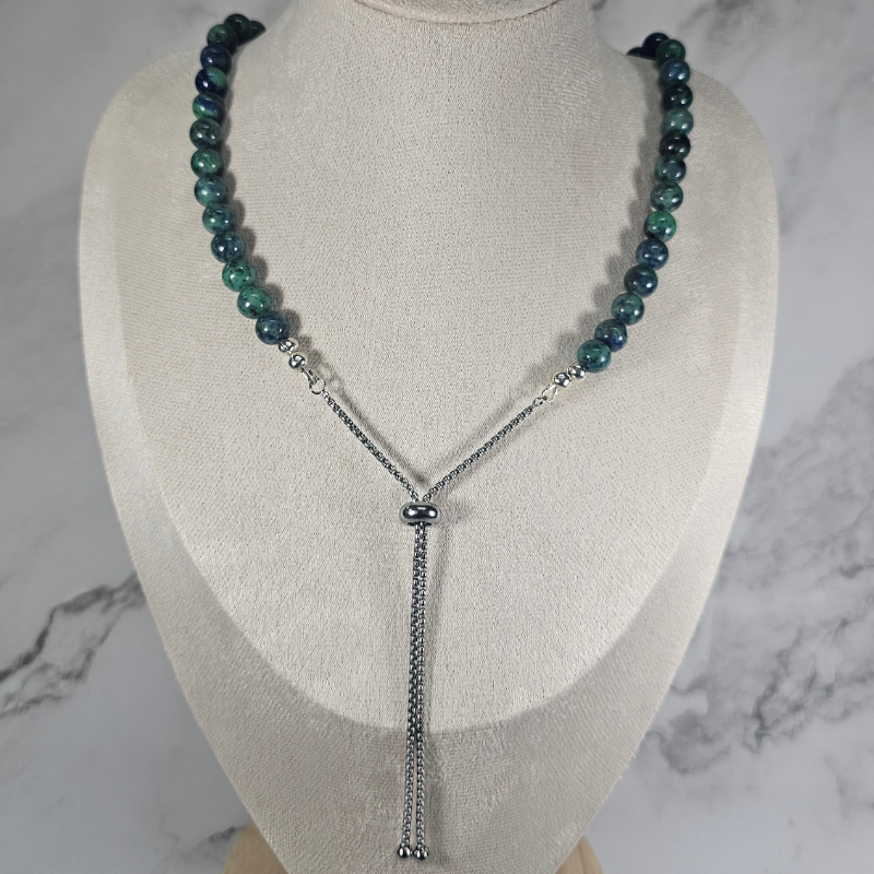 Necklace with green beads and silver chain on a mannequin bust against a marble background