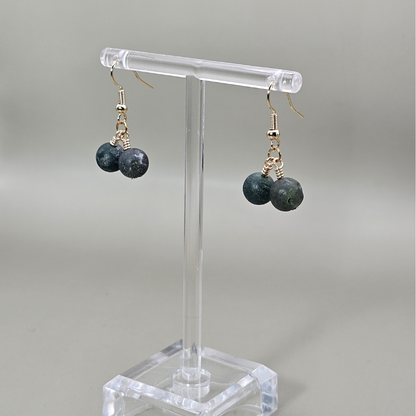 Earrings with green beads on a clear stand against a gray background