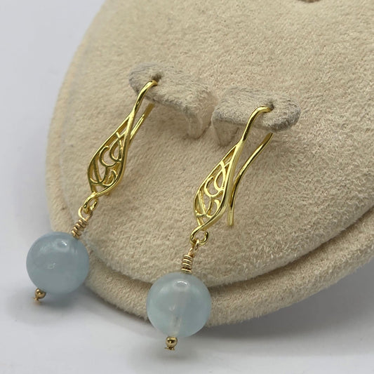 Gold earrings with green beads on a beige cushion