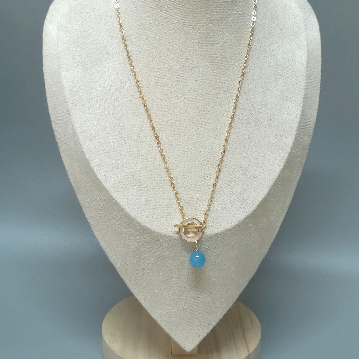 Gold necklace with aquamarine pendant on a white mannequin bust against a gray background