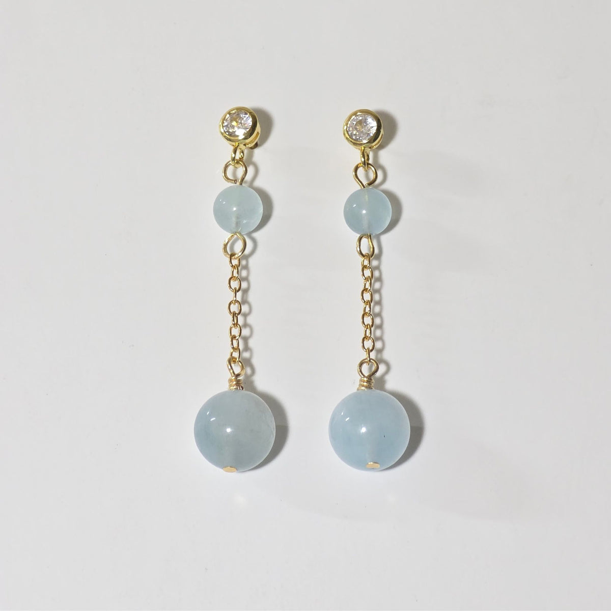 Pair of earrings with light blue gemstones and gold chains on a white background
