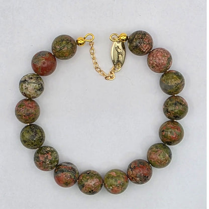 Bracelet with green and brown beads and gold clasp on a white background